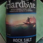 bag of Hardbite brand chips, Rock Salt & Vinegar with a beautiful sunset behind a surfer at Tofino, BC